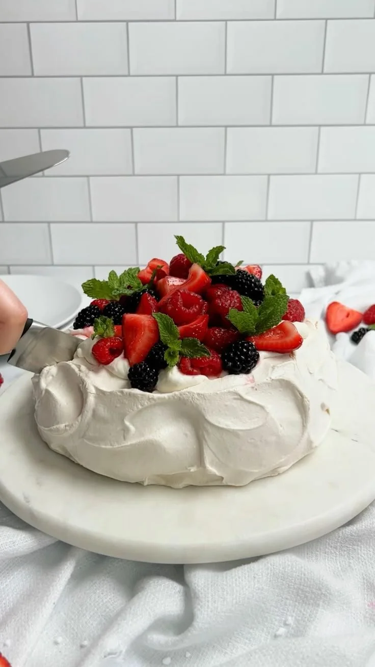 Delicious Berry Pavlova topped with fresh berries and cream on a white plate