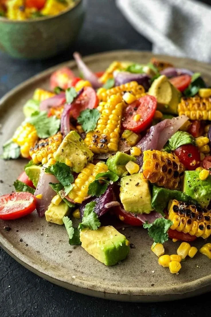 Charred corn avocado salad topped with roasted red onions in a colorful bowl