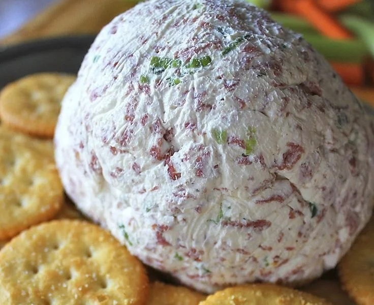 A delicious cheese ball displayed on a platter surrounded by crackers and vegetables.