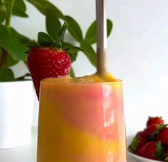 Healthy mango strawberry sunrise smoothie in a glass with fresh fruits
