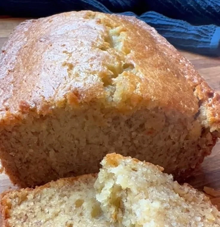 A loaf of old fashioned banana bread on a wooden cutting board with ripe bananas.